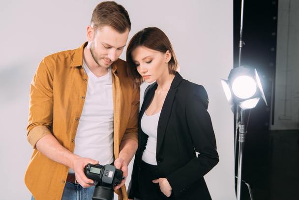Handsome photographer and elegant model looking at display of digital camera in photo studio  - Photo, Image