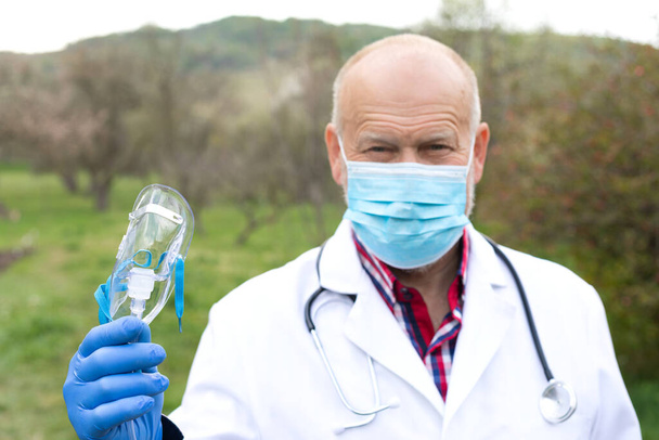 Portrait of senior male doctor with uniform and surgical mask posing outdoors - Foto, afbeelding