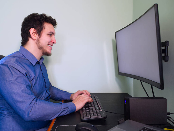 Un joven programador caucásico riéndose delante de la computadora. Concepto de teletrabajo. Cuarentena
. - Foto, imagen
