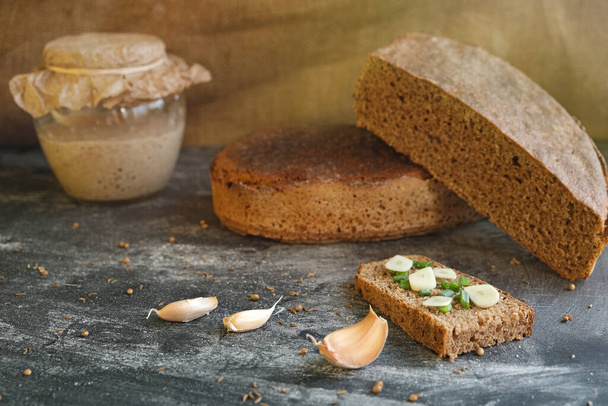 緑のタマネギのチャイブとクローブニンニクと新鮮な職人のパンの作品とまだ生活,ガラス瓶とローフ健康素朴な手作りライ麦全粒酵母フリーリーブンパン - 写真・画像