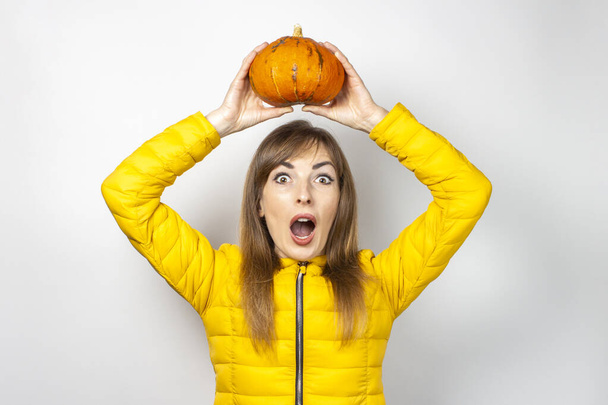 молода дівчина з переляканим обличчям тримає гарбуз над головою на світлому тлі. концепція Хеллоуїна, осінь, святкування
. - Фото, зображення