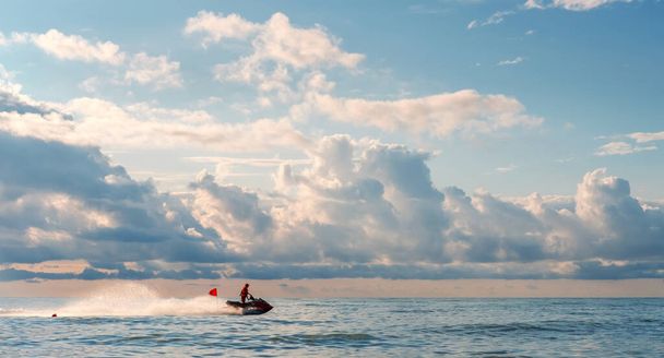 Záchranář vody hlídá mořské pobřeží na vodním skútru s červenou vlajkou, krásné oblačné pozadí oblohy - Fotografie, Obrázek