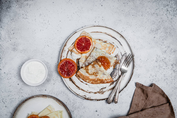 smażone naleśniki z kwaśną śmietaną i pomarańczami w talerzach na szarym tle, tradycyjna koncepcja śniadaniowa - Zdjęcie, obraz