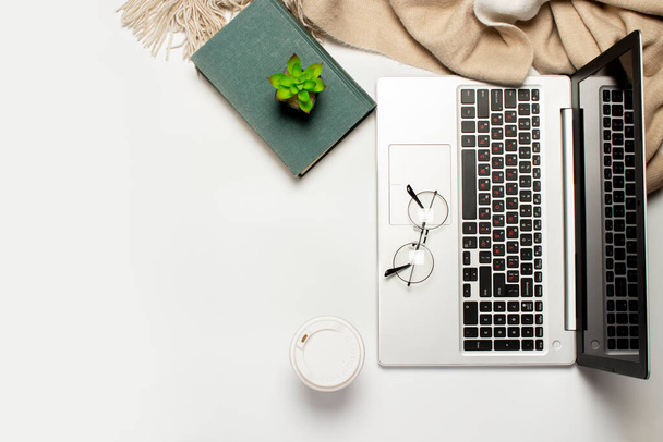 Freelancer werkruimte, laptop, plaid, kop met koffie op een licht witte achtergrond. Technologie concept, thuis werken, creatief proces. Vlakke lay, bovenaanzicht. - Foto, afbeelding