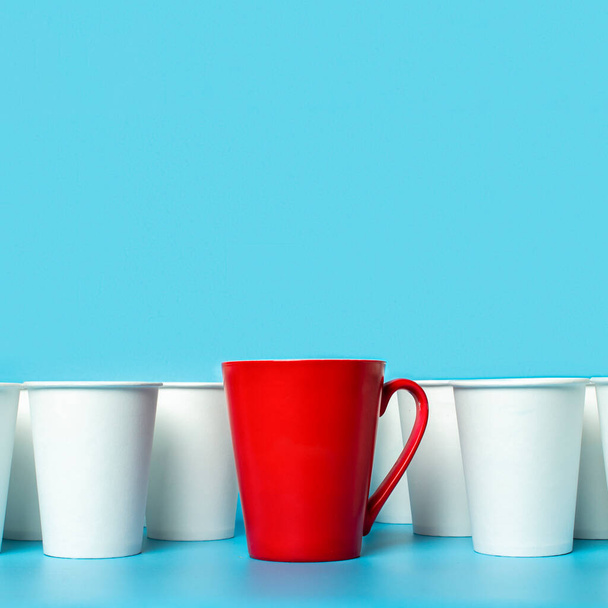 Красная чашка в окружении белых бумажных стаканчиков на синем фоне. Концепт босс, уникальная, дружелюбная команда. Копирование пространства
. - Фото, изображение