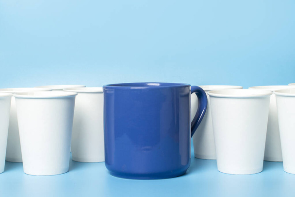 Large blue cup surrounded by white paper cups on a blue background. Concept boss, unique, friendly team, fimenism. Copy space. - Photo, Image