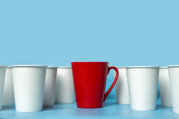Red cup surrounded by white paper cups on a blue background. Concept boss, unique, friendly team. Copy space. - Photo, Image