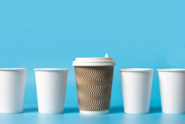 Large paper cup surrounded by white paper cups on a blue background. Concept boss, unique, friendly team, fimenism. Copy space. - Photo, Image