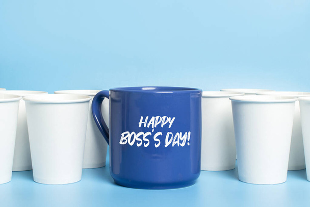 Large blue cup surrounded by white paper cups on a blue background. Concept boss, unique, friendly team, fimenism. Copy space. Added text Happy Boss's Day. - Photo, Image