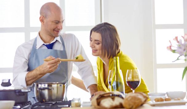 Улыбающаяся молодая пара готовит еду на кухне - Фото, изображение