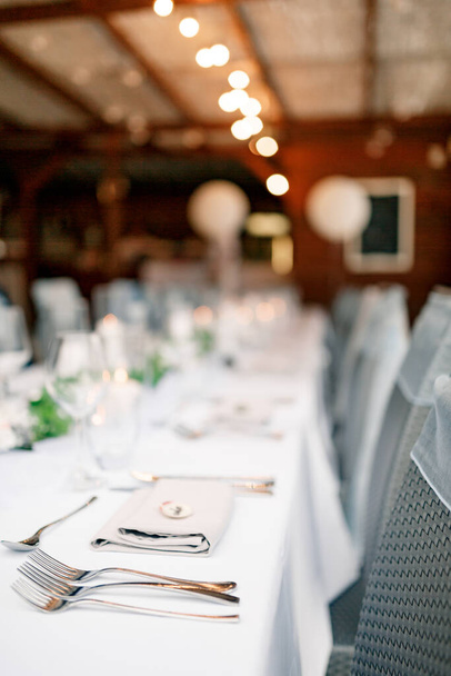 Close-up de uma mesa de jantar de casamento. Garfos em primeiro plano em uma toalha de mesa branca. Guirlanda sobre a mesa
 - Foto, Imagem