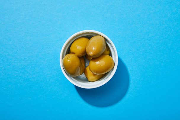top view of olives in bowl on blue colorful background - Zdjęcie, obraz