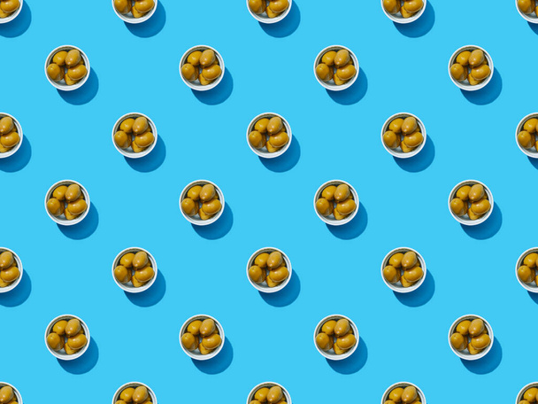κορυφαία άποψη των ελιών σε μπολ σε μπλε πολύχρωμο φόντο, απρόσκοπτη μοτίβο - Φωτογραφία, εικόνα