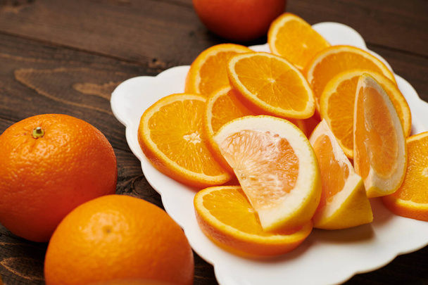 Frutta fresca di arancia intera e affettata su un piatto, fondo di legno scuro - cibo naturale e sano
. - Foto, immagini
