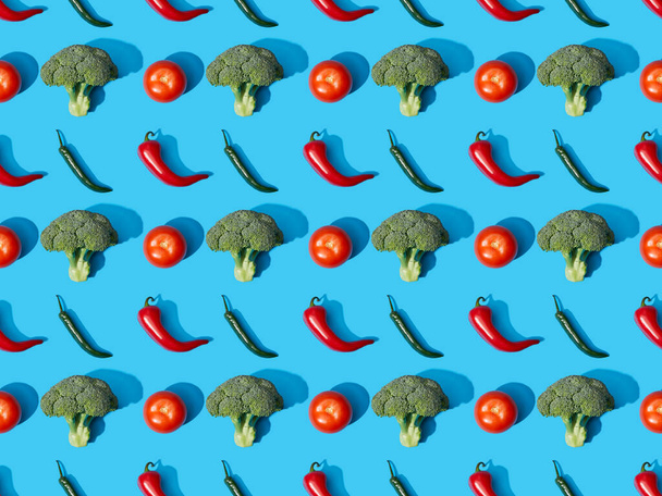 top view of fresh green broccoli, chili peppers and tomatoes on blue background, seamless pattern - Photo, Image