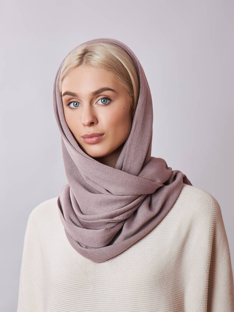 European Muslim woman with a blonde hair in a headscarf shawl dressed on her head. Beautiful girl in sweater with soft skin, natural cosmetics - Zdjęcie, obraz