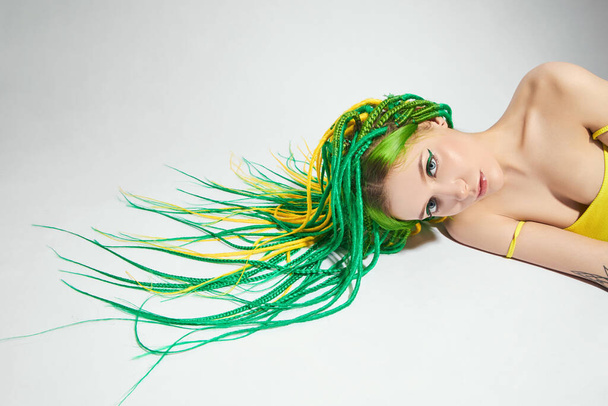 Portrét ženy s kreativně zbarvenými vlasy v zelené a žluté barvě. Barevné světlé dredy, krásný moderní make-up - Fotografie, Obrázek