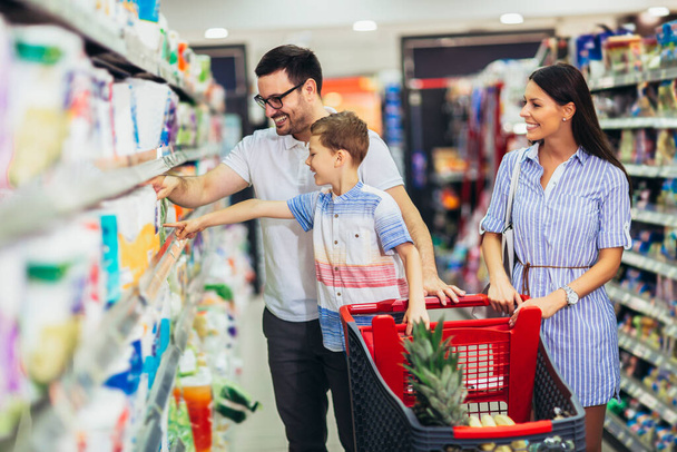 Счастливая семья с ребенком и покупка продуктов в продуктовом магазине или супермаркете - Фото, изображение