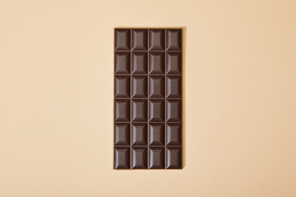 top view of sweet dark chocolate bar on beige background - Zdjęcie, obraz