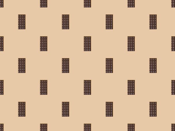 top view of sweet dark chocolate bars on beige background, seamless pattern - Foto, imagen
