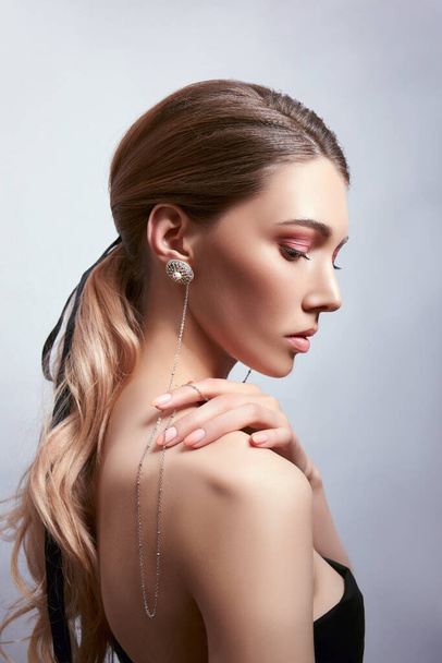 Πορτραίτο ομορφιάς μιας γυναίκας με μακριά μαλλιά, σκουλαρίκια στα αυτιά και ακριβά κοσμήματα στα χέρια της - Φωτογραφία, εικόνα