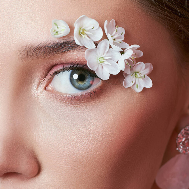 Primavera mulher olho maquiagem com flores brancas. Maquiagem de olho de beleza floral criativo. Cosmético de pestanas com flores de verão
 - Foto, Imagem