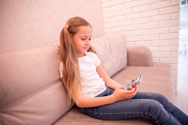 Casual baby sitting on a couch at home playing and touching a mobile phone - Zdjęcie, obraz