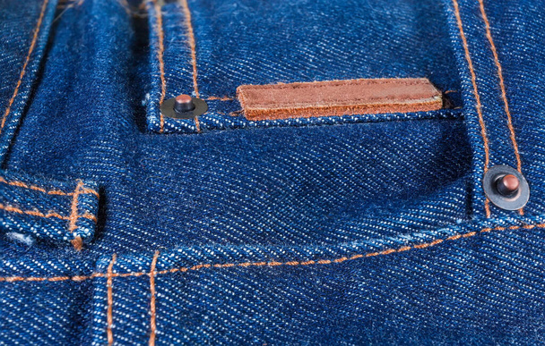 Πριτσίνια χαλκού και ραμμένο κενό μικρό παχύ δέρμα ετικέτα σε ένα μπλε τζιν, close-up σε επιλεκτική εστίαση - Φωτογραφία, εικόνα