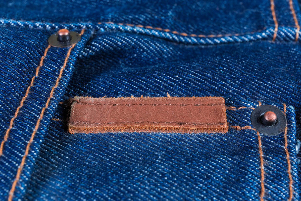 Kupfernieten und genähtes leeres kleines dickes Lederetikett auf einer blauen Jeans, Nahaufnahme in selektivem Fokus - Foto, Bild