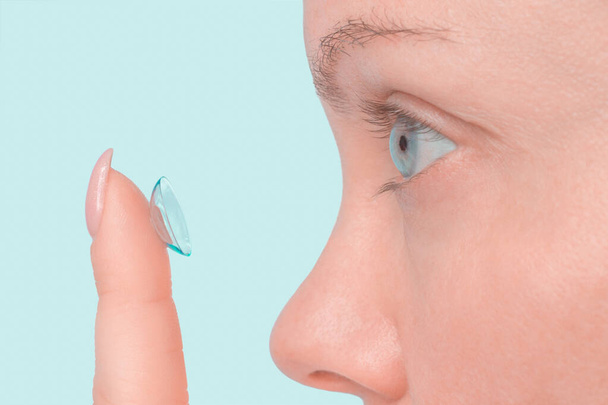 Close up on woman applying contact lens on blue background, without cosmetics - Foto, immagini