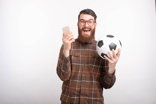 Exited man is holding his phone and soccer or football ball. - Photo, Image