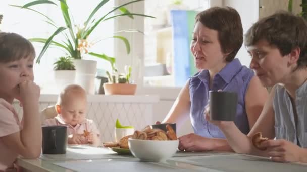 Eine homosexuelle lesbische Familie mit zwei Kindern und Müttern sitzt in der Küche an einem Tisch und frühstückt. Lebensstil. - Filmmaterial, Video