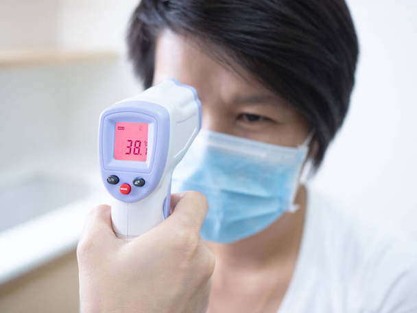 Woman doctor holding medical infrared forehead thermometer checking body temperature of coronavirus infected patients in quarantine area, showing high fever. Covid-19 and coronavirus concept. - Foto, Bild