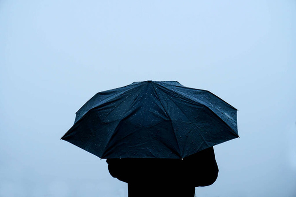 Alone man standing out in rain with an umbrella - 写真・画像