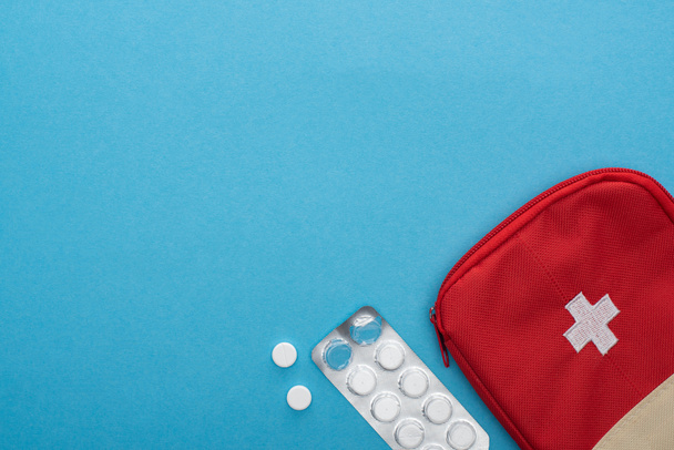 вид зверху таблеток у блістерній упаковці та червоний набір першої допомоги на синьому фоні
 - Фото, зображення