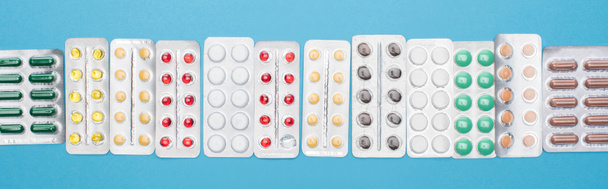 bovenaanzicht van kleurrijke pillen in blisterverpakkingen op blauwe achtergrond, panoramische oriëntatie - Foto, afbeelding