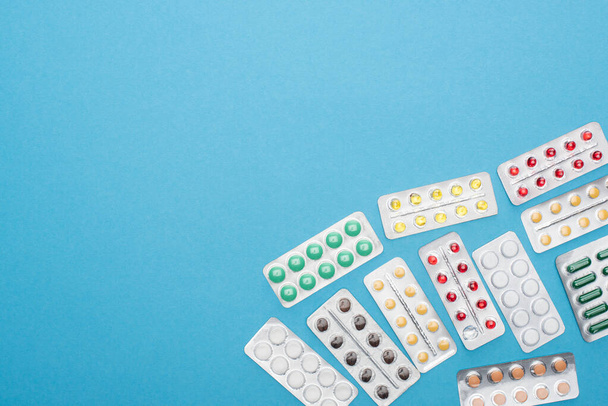 top view of colorful pills in blister packs on blue background - Foto, afbeelding
