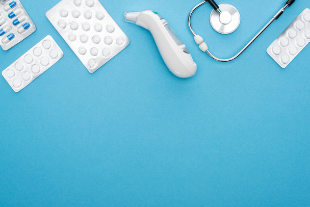 bovenaanzicht van pillen in blisterverpakkingen, stethoscoop en oorthermometer op blauwe achtergrond, horizontaal beeld - Foto, afbeelding