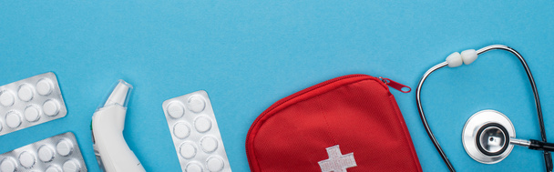 bovenaanzicht van pillen in blisterverpakkingen, stethoscoop, verbanddoos en oorthermometer op blauwe achtergrond, horizontaal beeld - Foto, afbeelding