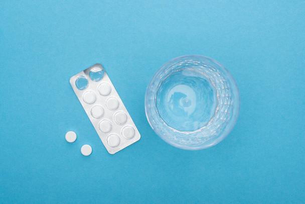 top view of pills in blister pack, glass of water on blue background - Valokuva, kuva