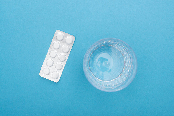 top view of pills in blister pack, glass of water on blue background - Zdjęcie, obraz