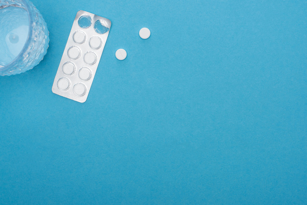 top view of pills in blister pack, glass of water on blue background - Photo, Image