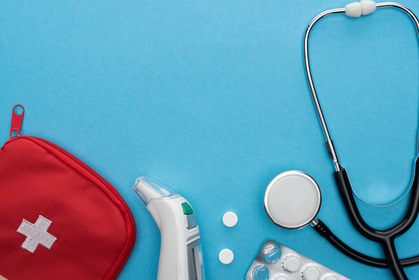 Ansicht von Pillen in Blisterverpackung, Stethoskop, Verbandskasten und Ohrthermometer auf blauem Hintergrund - Foto, Bild