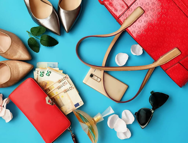  donne vestiti accessori rosso borsetta portafoglio con euro soldi occhiali da sole, telefono e profumo aroma su sfondo blu moda business sfondo
  - Foto, immagini
