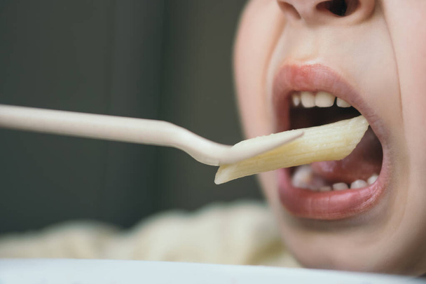 Nahaufnahme eines kleinen Jungen, der Penne-Pasta mit Gabel isst - Foto, Bild