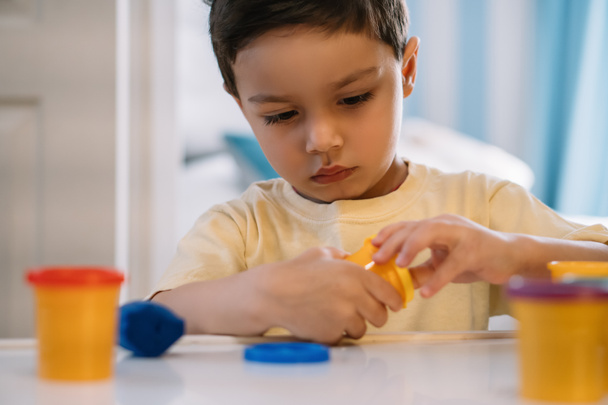 selective focus of attentive, adorable boy opening container with  plasticine - Photo, Image