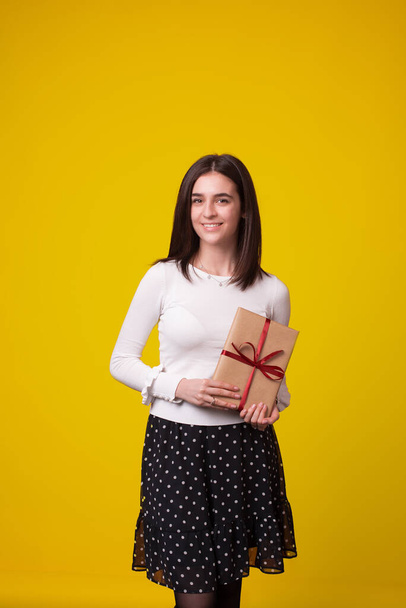 Foto vertical de una chica de pie presentando un regalo en sus manos
. - Foto, imagen