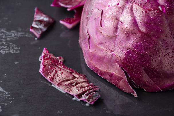 Top view of red cabbage wet on its outer side, with pieces, on black slate, horizontal - Photo, Image