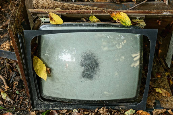 afval van een gebroken oude kapotte televisie met een grijze beeldbuis in de straat in geel gevallen bladeren - Foto, afbeelding