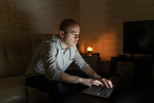 Attractive Caucasian man sitting at home and using a laptop computer for work at night - Fotografie, Obrázek